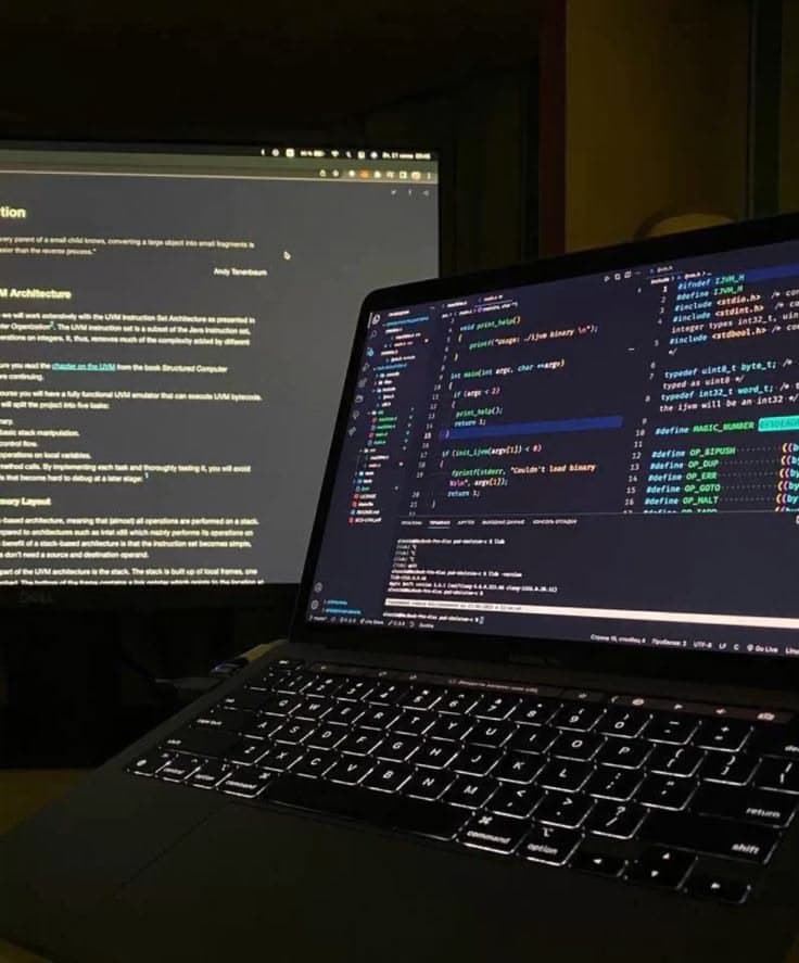 A laptop showing source code next to reference notes on a second screen.